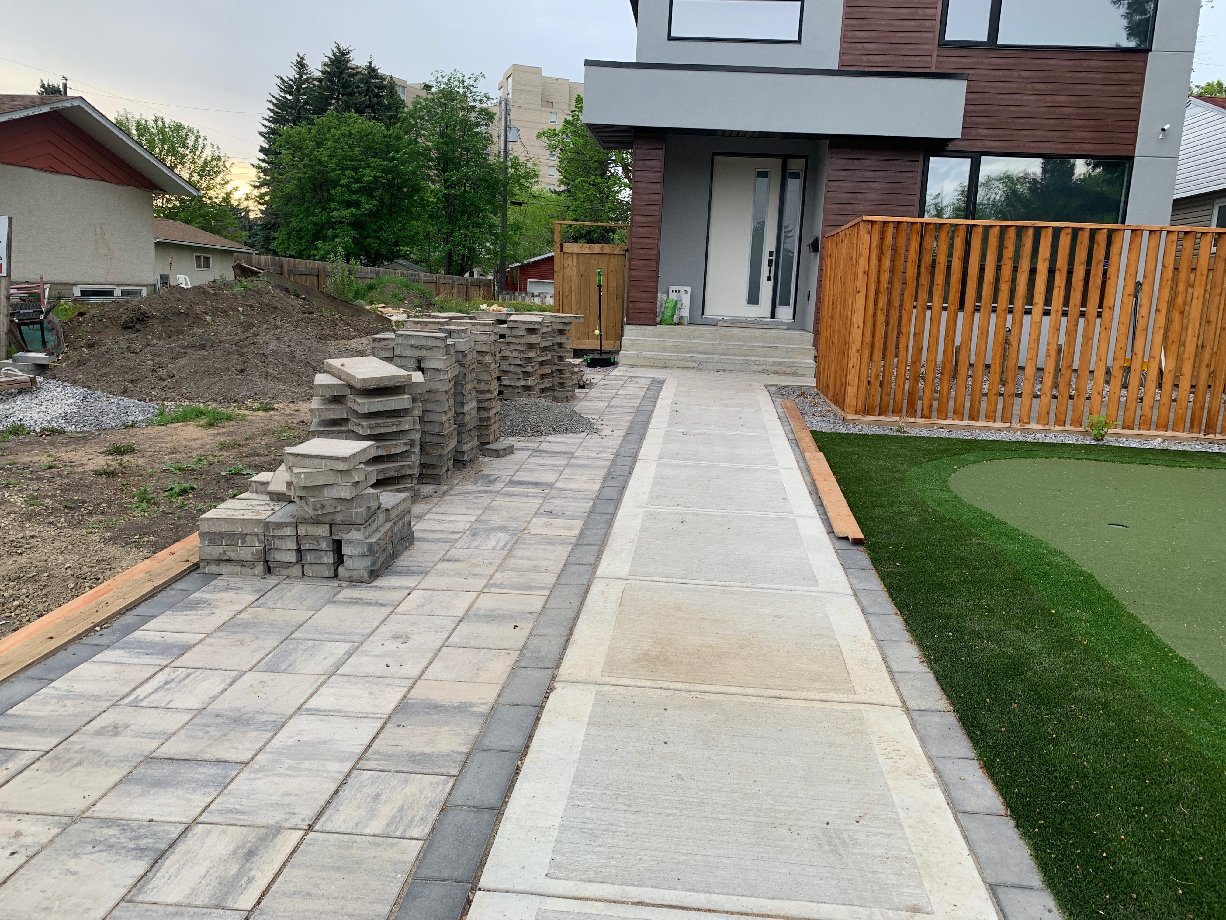 Large paver driveway under construction with cedar fence